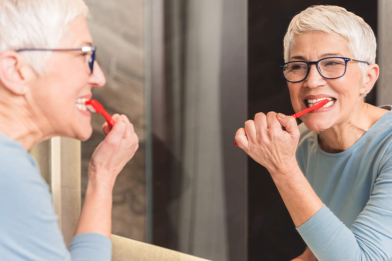 Mirror reflection of beautiful mature woman brushing her teeth with red toothbrush, Daily dental hygiene routine concept